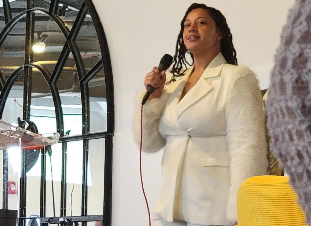 woman wearing white suite and speaking at microphone.